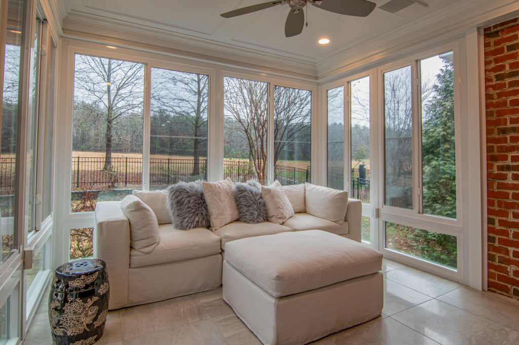Cozy sunroom featuring a modern white sofa and large windows with a serene outdoor view.